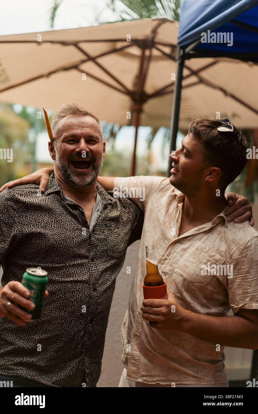 Due uomini che ridono insieme a un drink a una festa all'aperto Foto Stock