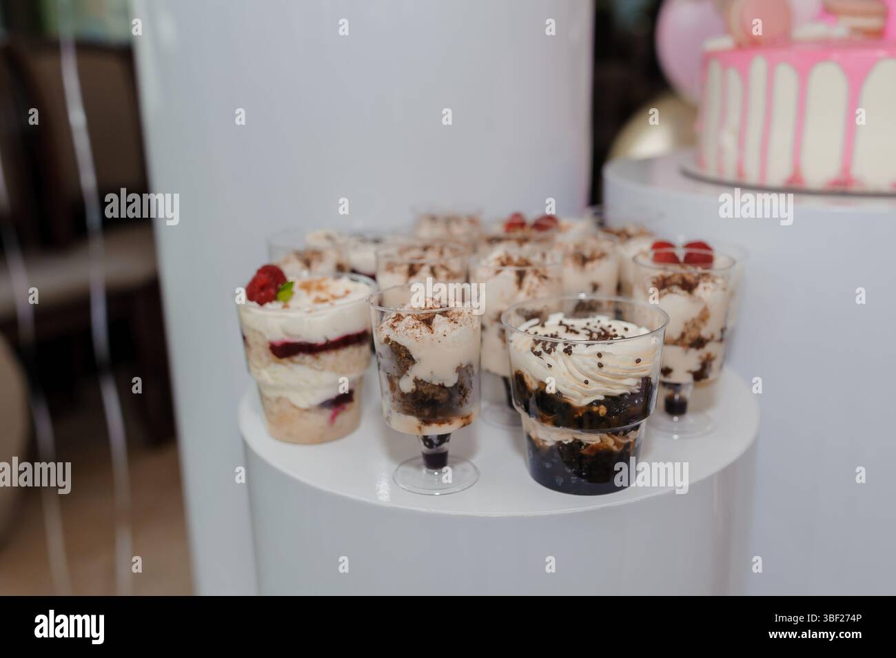 Viene presentato un tavolo da dessert splendidamente organizzato, con diverse piccole tazze di plastica riempite con una ricca mousse di cioccolato, ricoperte di frutti di bosco e. Foto Stock