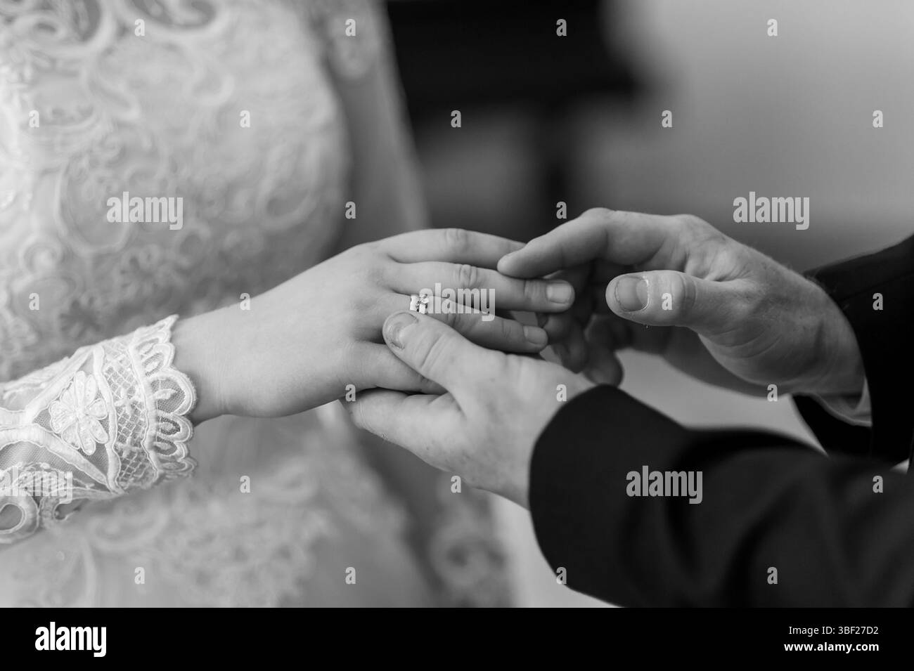 Una foto in bianco e nero in primo piano evidenzia lo scambio di fedi nuziali, mentre la mano dello sposo tiene delicatamente la sposa mentre si infila la banda, sig Foto Stock