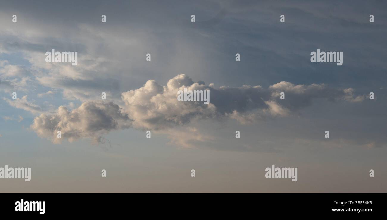 Composición que captura la inmensidad del cielo, una majestuosa formación de nubes cúmulos domina el centro, destacando por su volumen y textura. Foto Stock