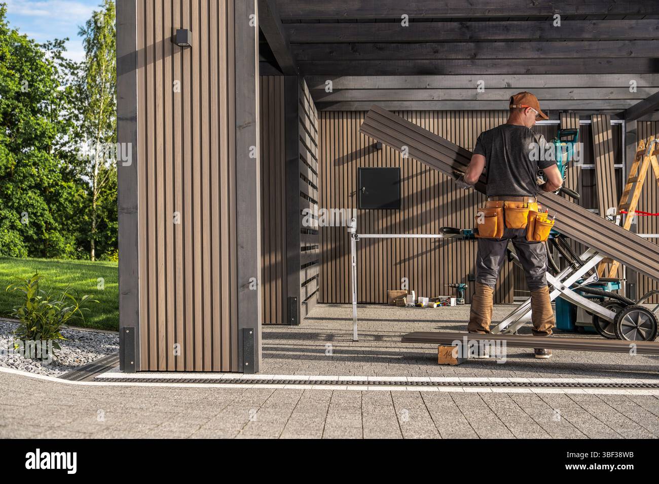 Un falegname maneggia meticolosamente pannelli di lamella in legno in un'elegante area di lavoro all'aperto, mostrando maestria artigianale e attenzione ai dettagli in un ambiente luminoso Foto Stock