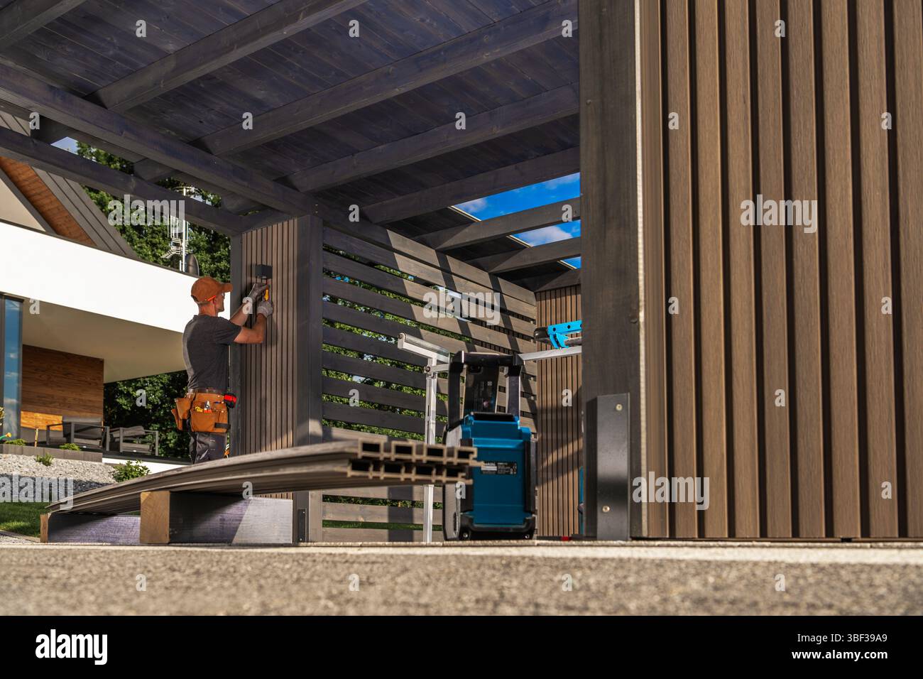 Un lavoratore esperto sta installando l'apparecchio di illuminazione in una struttura esterna contemporanea utilizzando vari strumenti. La luce del giorno aumenta l'attività A. Foto Stock