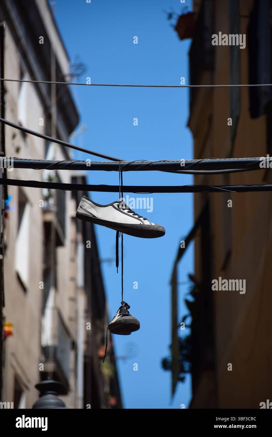Scarpe appese in alto su linee elettriche tra gli edifici di Barcelona Street Foto Stock