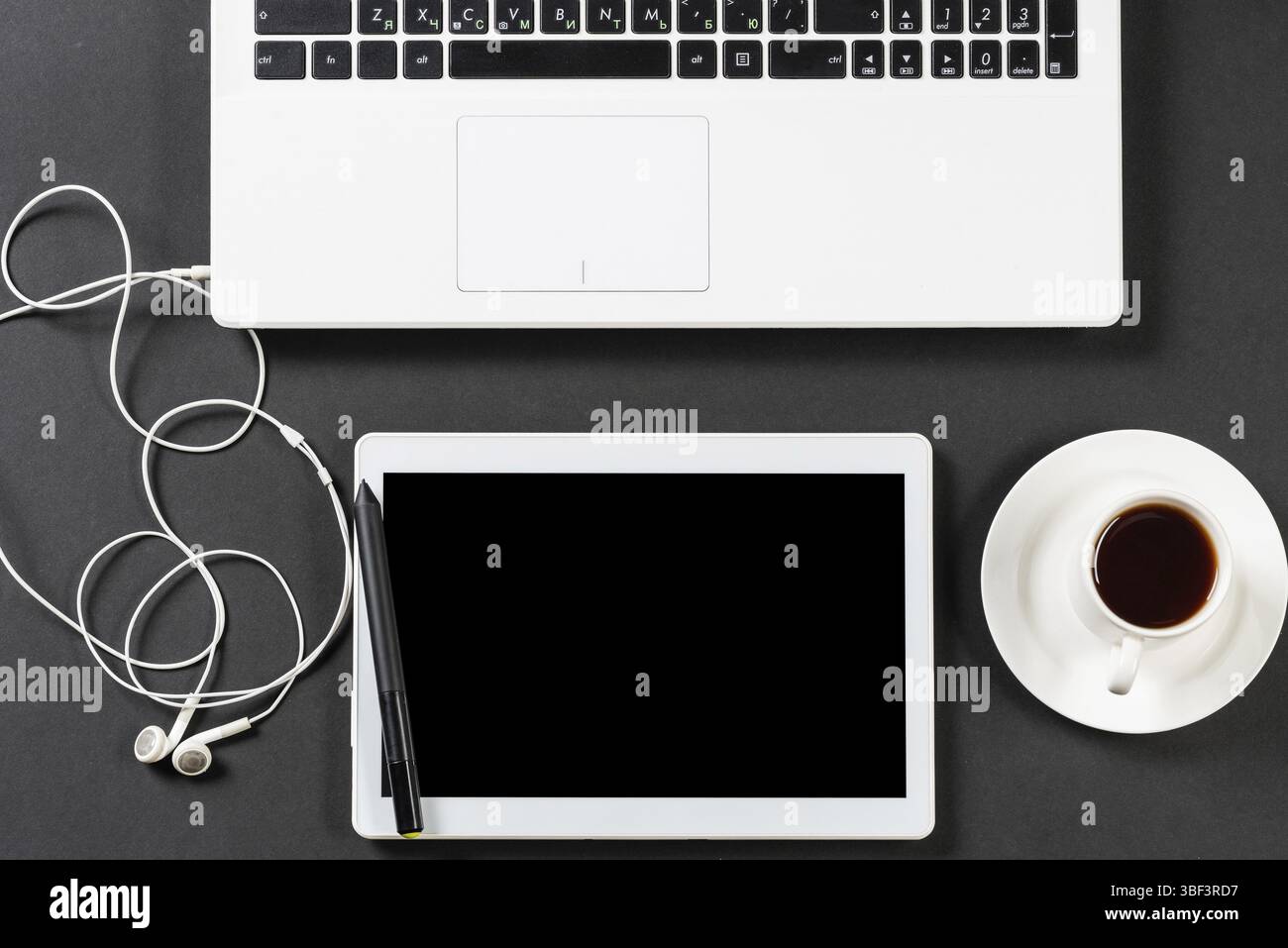 Natura morta del luogo di lavoro in ufficio organizzato con laptop e tazza di caffè. Superficie nera piatta con tablet computer e cuffie. Contemporaneità della vista dall'alto Foto Stock