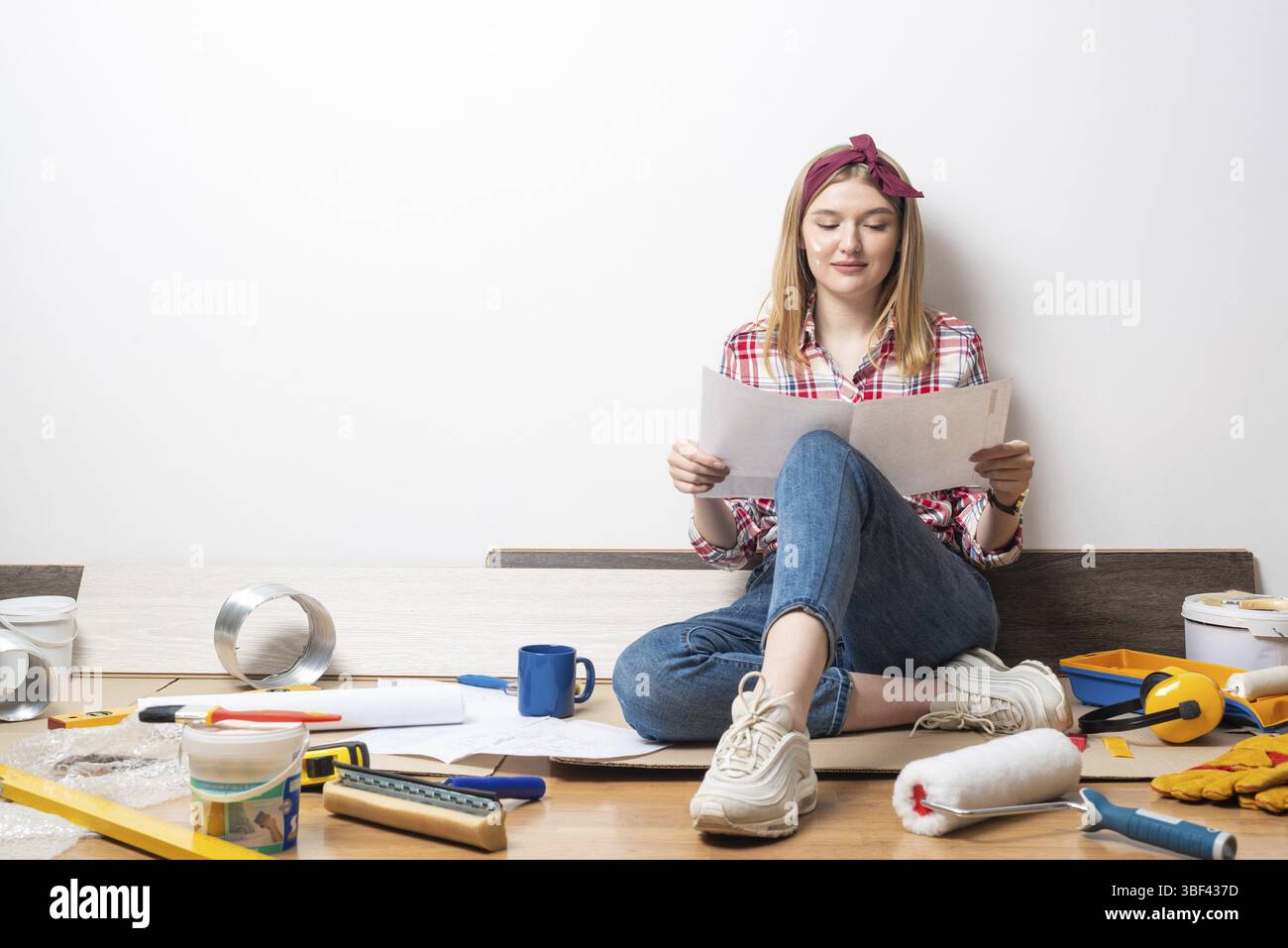 Ragazza sorridente seduta sul pavimento e con un progetto di carta. Ristrutturazione di abitazioni e riprogettazione di interni. Utensili e materiali da costruzione per l'edilizia. Foto Stock