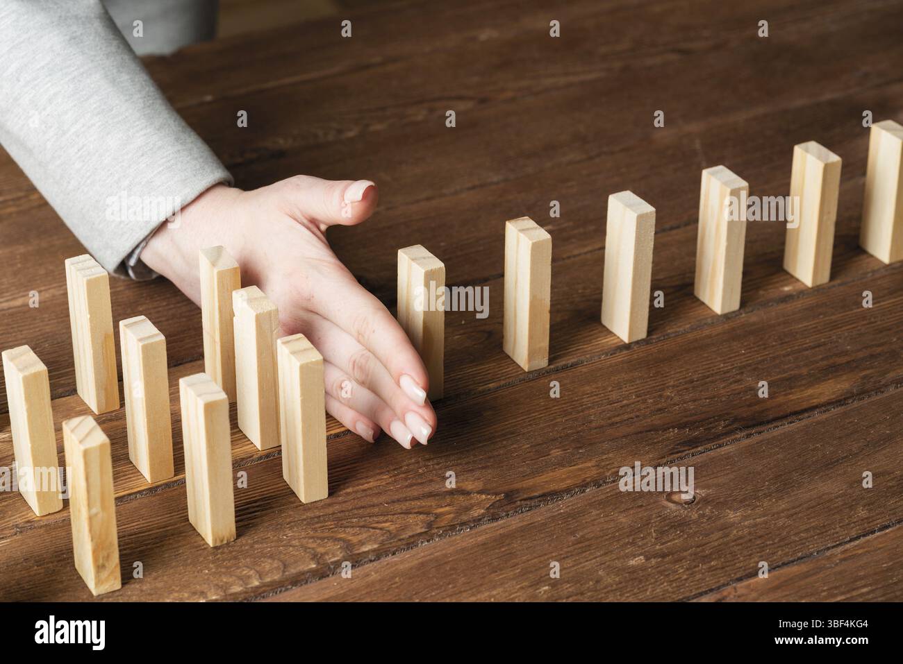 Donna d'affari blocca l'effetto domino. Assistenza aziendale, gestione dei rischi e situazione di stabilizzazione. Concetto di intervento in processo con blocco in legno Foto Stock