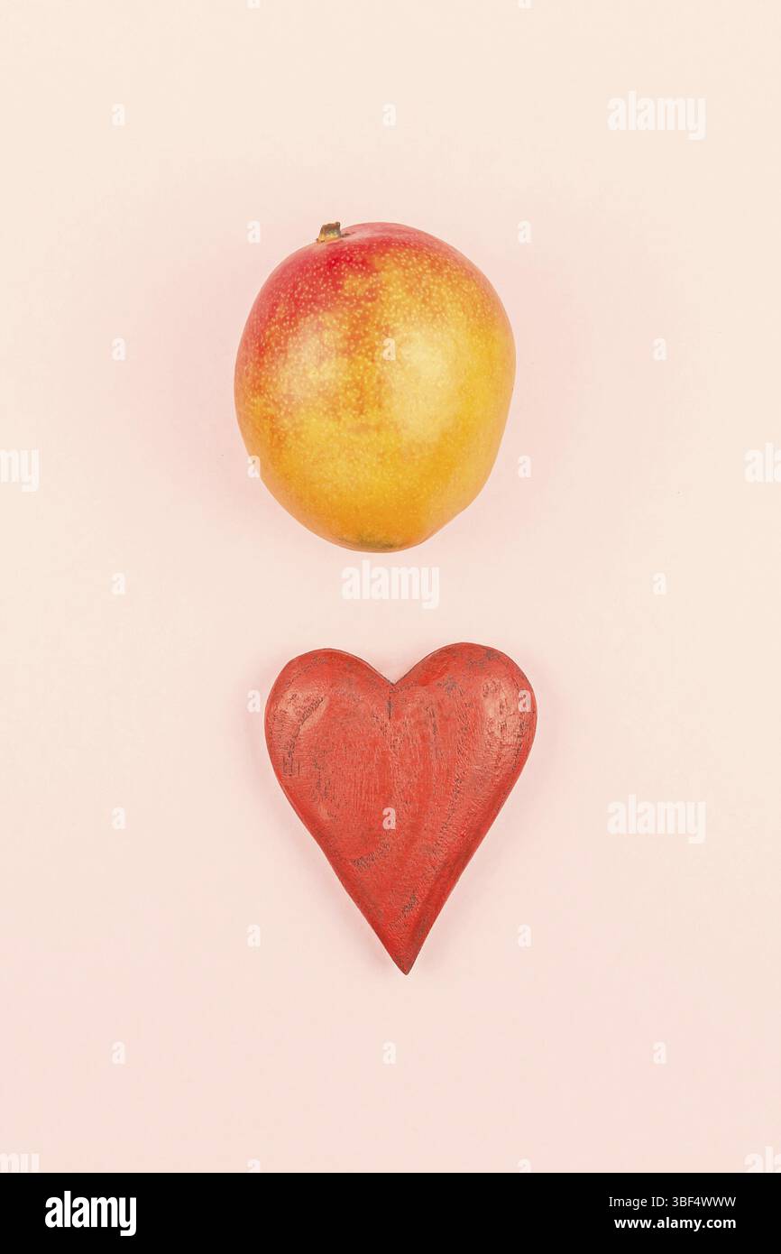 Mango Fruit in creativi concettuale vista superiore piatta composizione laici rosso con cuore in legno isolato su sfondo rosa in stile minimal con copia spazio. M Foto Stock