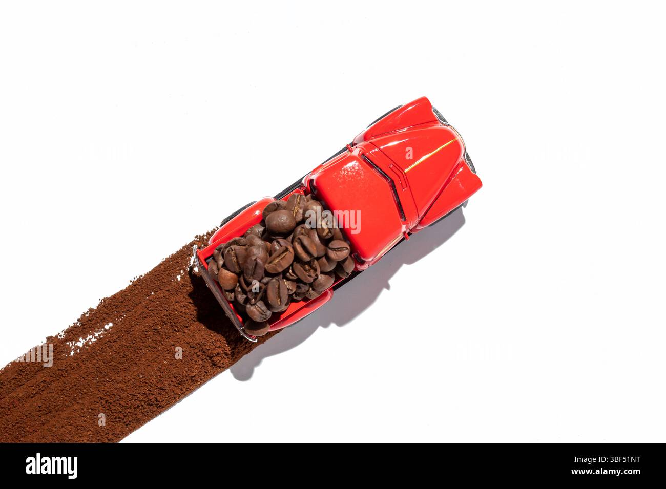 Chicchi di caffè in un camion giocattolo rosso sulla strada del caffè macinato. Concetto di trasporto minimalista Foto Stock