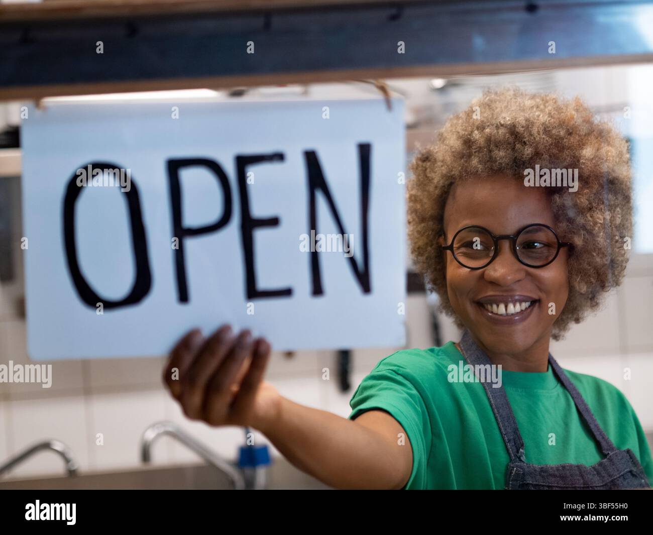 Donna africana sorridente con capelli afro che apre il suo piccolo ristorante Foto Stock