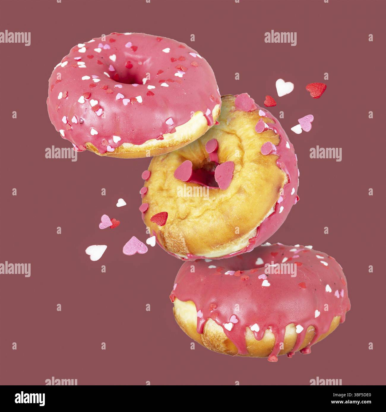 Ciambelle in glassa di zucchero rosa con cuori, cibo volante Foto Stock