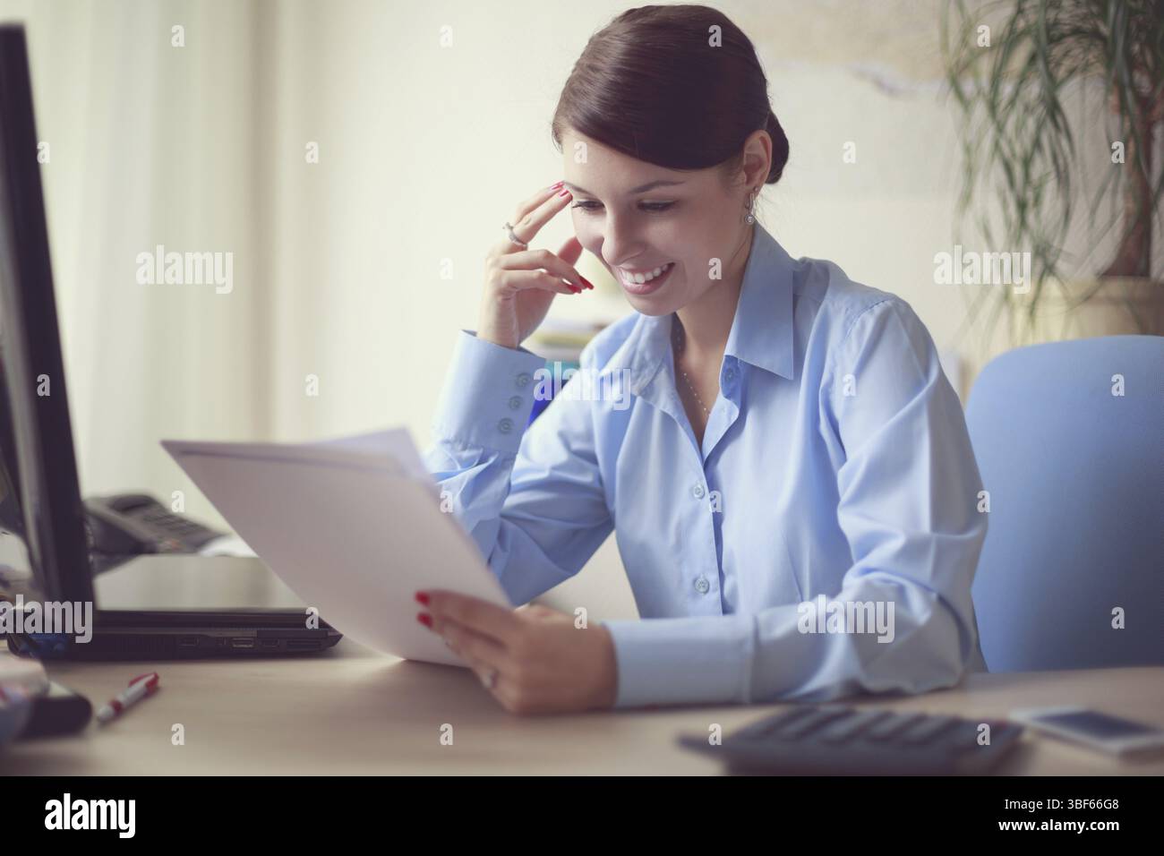 Ritratto di una giovane donna d'affari caucasica in camicia blu nel suo ufficio che legge i documenti Foto Stock
