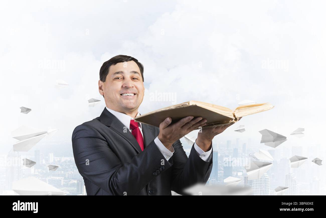 Happy businessman tenendo aperte vecchio libro. Uomo sorridente in tuta in piedi sul centro di sfondo con battenti piani della carta. Avvocato in possesso di grandi regula legale Foto Stock