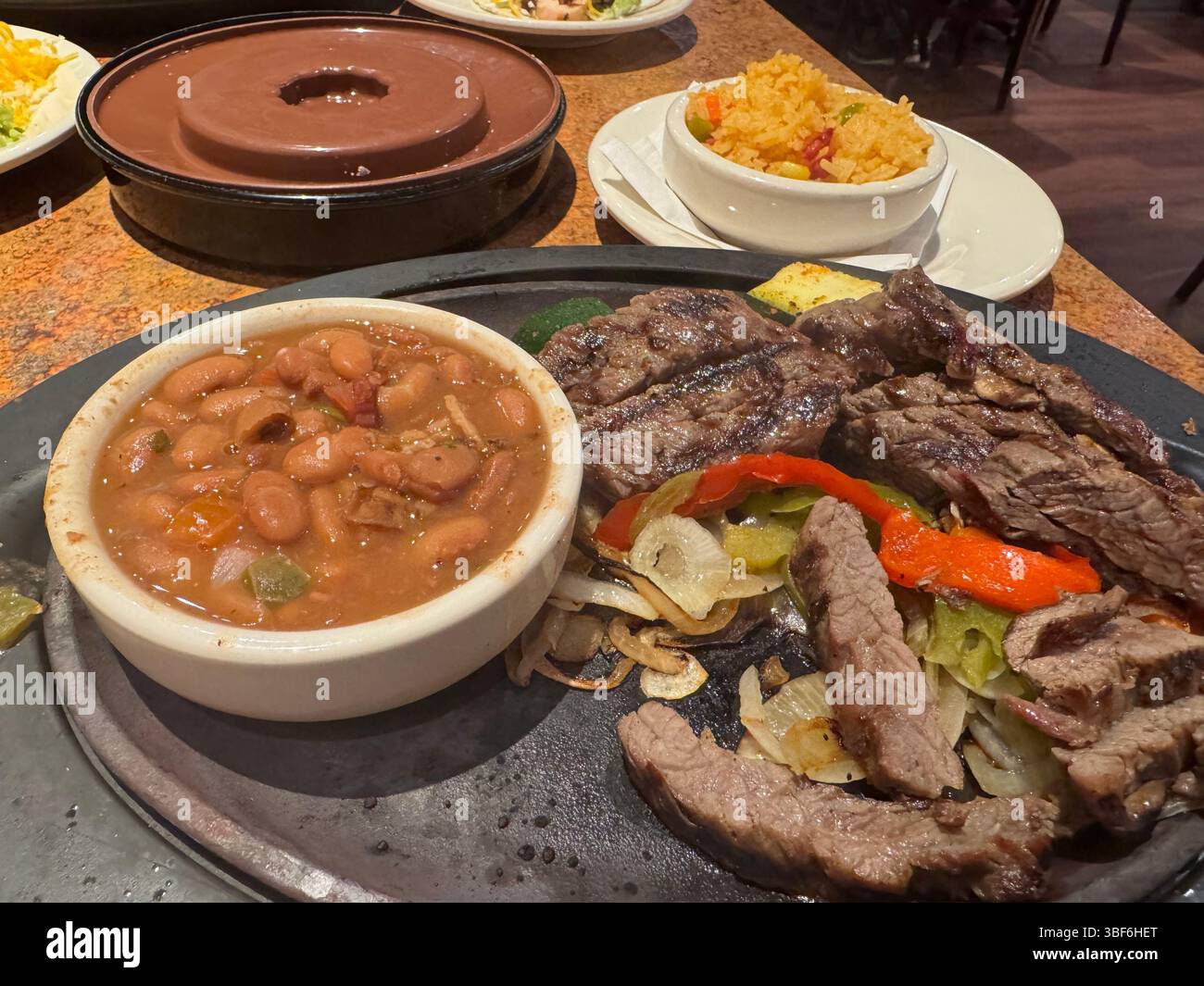 Esposizione di piatti messicani, fajitas, con cipolle saltate, manzo e peperoni con contorni di fagioli Pinto e riso messicano, in un ristorante, USA. Foto Stock