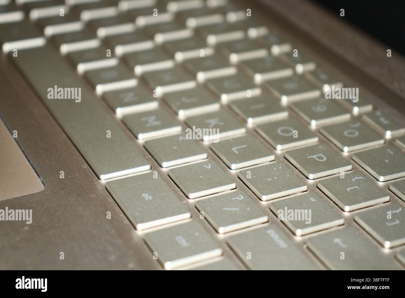 Tastiera color oro di un notebook con sfondo sfocato e luce intensa su una superficie. Foto Stock