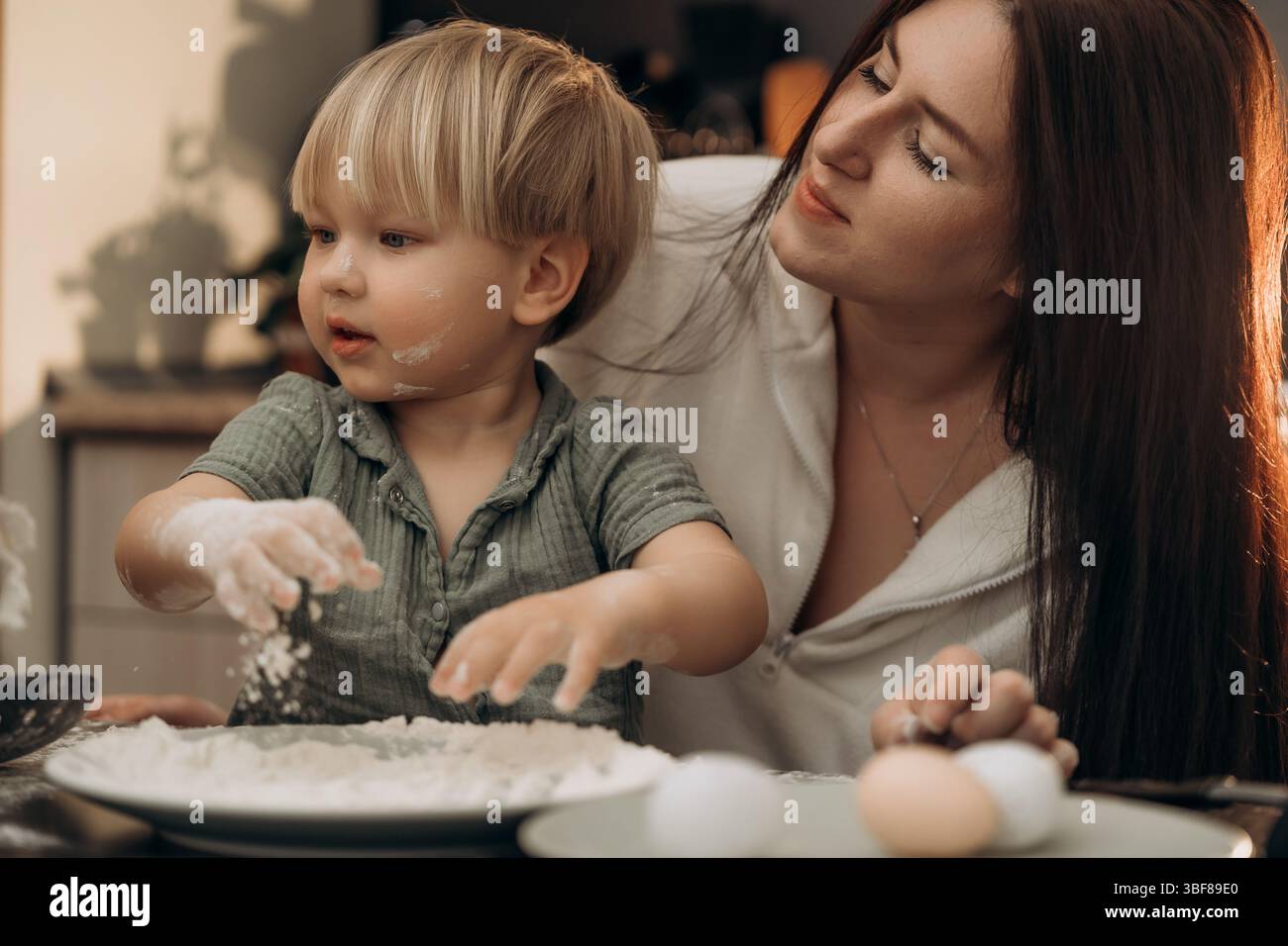 Il bambino esplora la farina con la madre che guarda catturando delicatamente i ricordi caldi dell'infanzia la famiglia si lega attraverso la cucina sensoriale gioca con la consapevolezza dei genitori e. Foto Stock