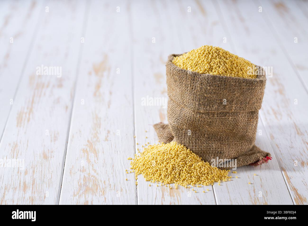 Grani gialli di miglio organici in sacchetti. Sacco con grani organici di miglio. Chicchi organici di miglio in sacchetto e mucchio di chicchi di miglio. Foto Stock