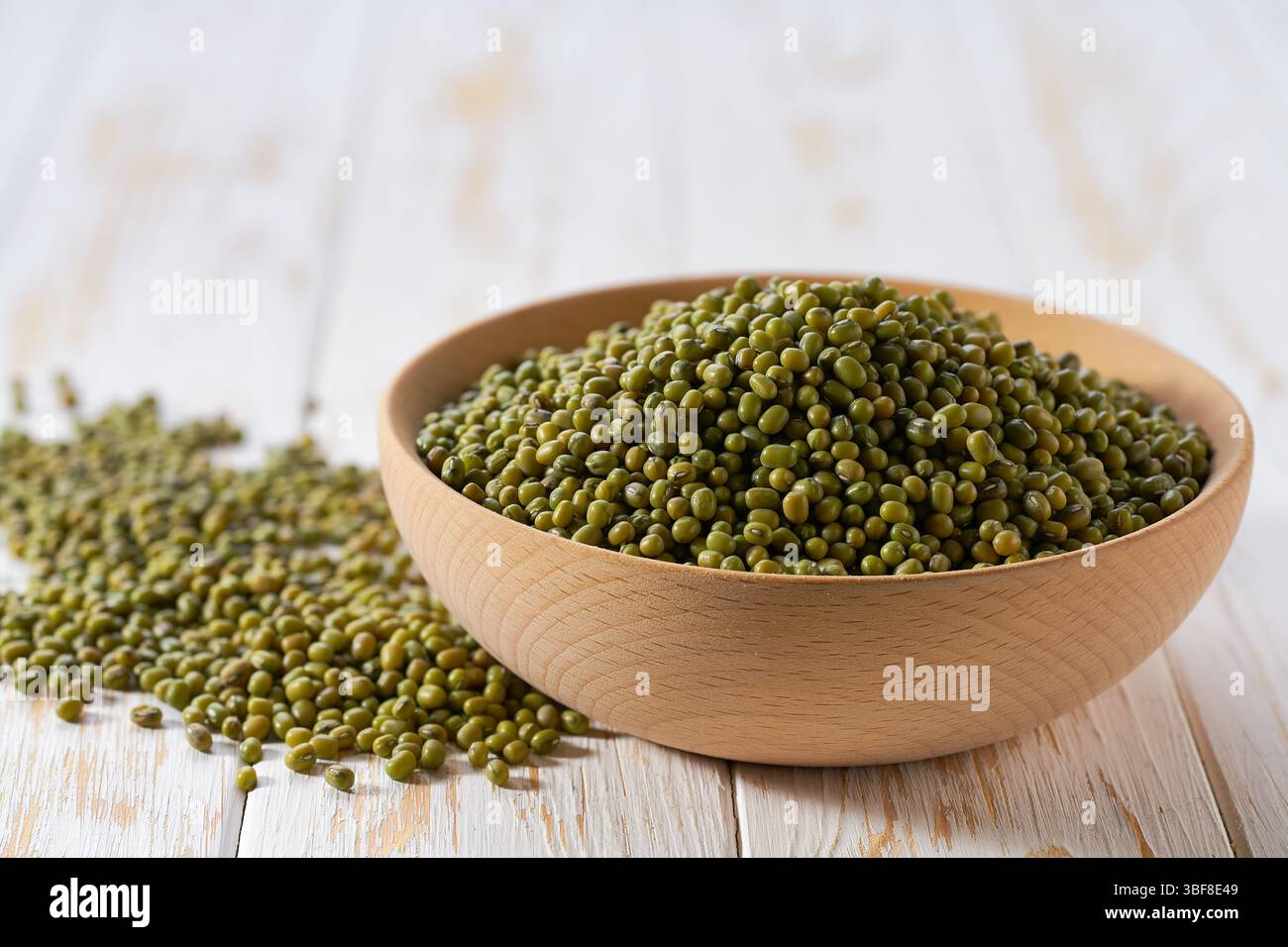 I fagioli di mughetto sono sparsi fuori dalla ciotola di legno su un tavolo leggero, con messa a fuoco selettiva. Foto Stock