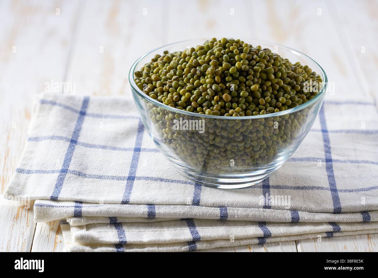 Fagioli verdi mung in un recipiente di vetro trasparente su un tavolo leggero, messa a fuoco selettiva. Foto Stock