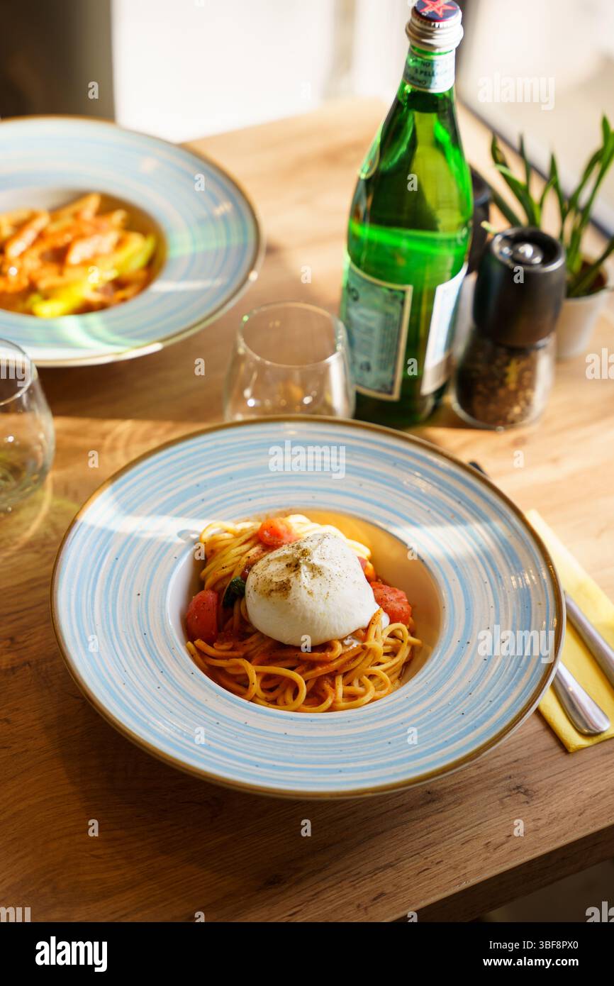 Primo piano di spaghetti conditi con burrata intera, serviti in un ricco sugo di pomodoro con pomodori ciliegini e basilico fresco. Un gourmet italiano Foto Stock