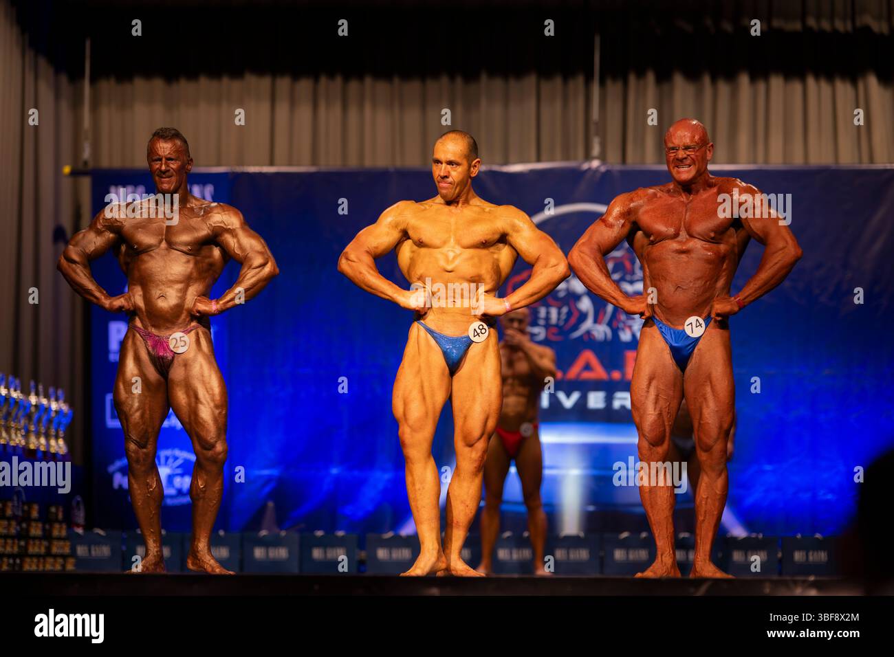 , Deutschland, Rheinland Pfalz, Limburgerhof, 31.05.2025, Drei männliche allestitore posieren Synchron auf einer Bühne während eines Bodybuilding-Wet Foto Stock