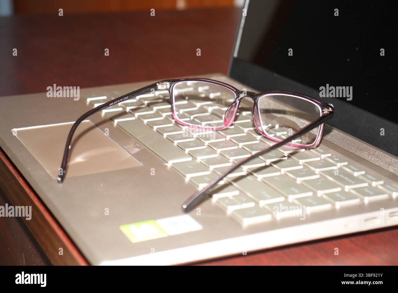 Un paio di occhiali si trova sulla tastiera di un notebook con sfondo sfocato. Il laptop è in posizione di riposo e si trova in posizione di spegnimento. Foto Stock