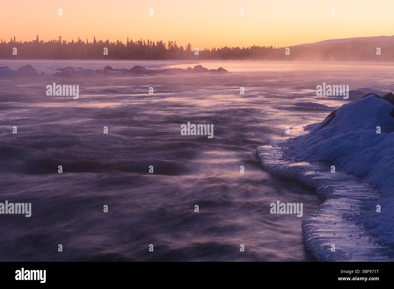 Un tranquillo tramonto invernale su un fiume in Norvegia rivela lisce formazioni di ghiaccio lungo la riva e la nebbia che si innalza dalla superficie dell'acqua. I colori tenui Foto Stock