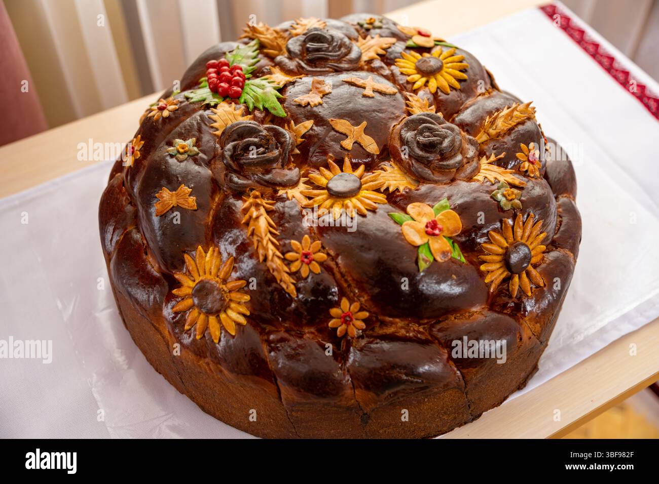 Un pane rotondo per le vacanze presenta decorazioni floreali e disegni realizzati con impasto. Presenta girasoli, rose e frutti di bosco, presentando un vib Foto Stock