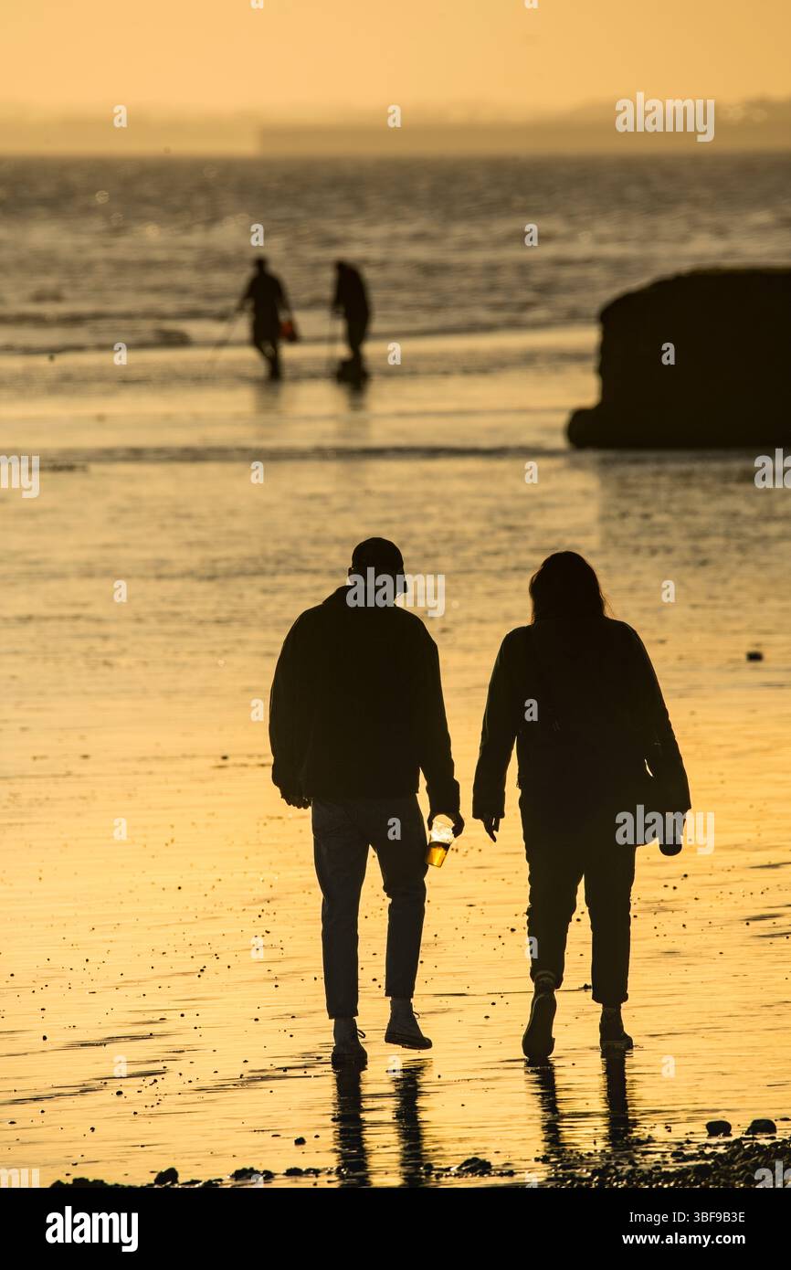 Coppia che cammina insieme sulla sabbia nella spiaggia di Brighton con la bassa marea. Inghilterra. Silhouette. Brighton, Inghilterra, Regno Unito. Foto Stock