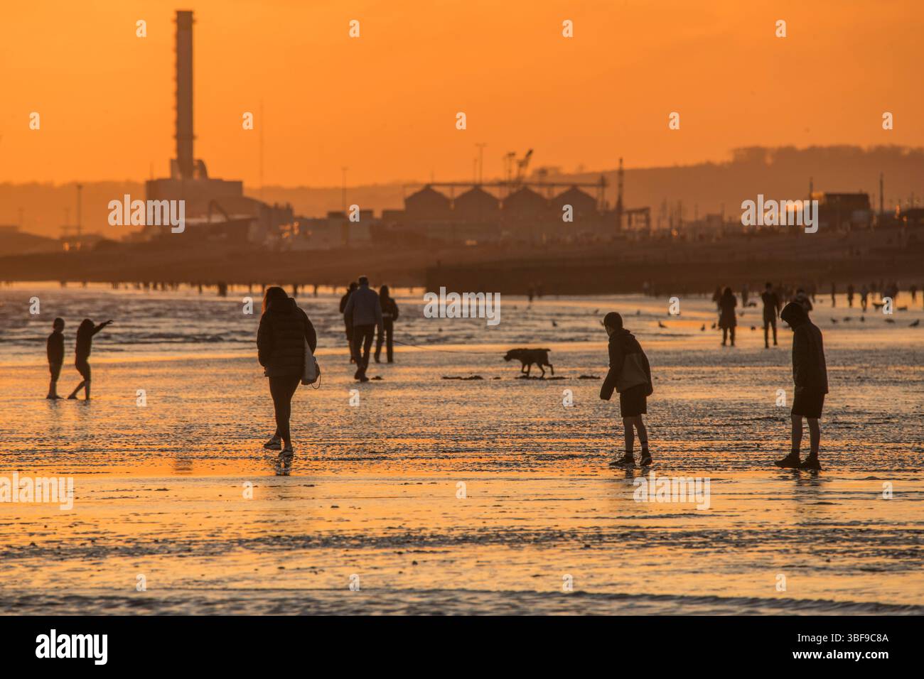 Il sole che tramonta dalla spiaggia di Brighton si affaccia su Hove verso la centrale elettrica di Shoreham. Gente che si gode la bassa marea al tramonto. Brighton e Hove, Inghilterra, Regno Unito Foto Stock