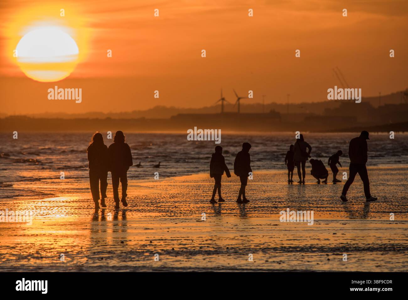 Il sole che tramonta visto dalla spiaggia di Brighton. Gente che si gode la bassa marea al tramonto. Fotografato dalla spiaggia di Brighton che guarda a ovest attraverso Hove. Brighton e Hove, Inghilterra, Regno Unito Foto Stock