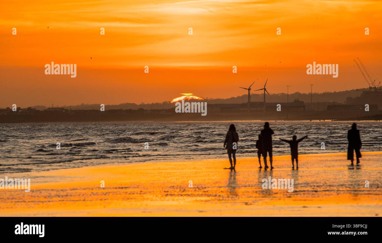 Tramonto oltre Shoreham. Fotografato dalla spiaggia di Hove che guarda a ovest. Enigmatico "flash verde" visibile in cima al sole visibile negli ultimi secondi del tramonto. Gente che si sveglia sulla spiaggia con la bassa marea. Foto Stock