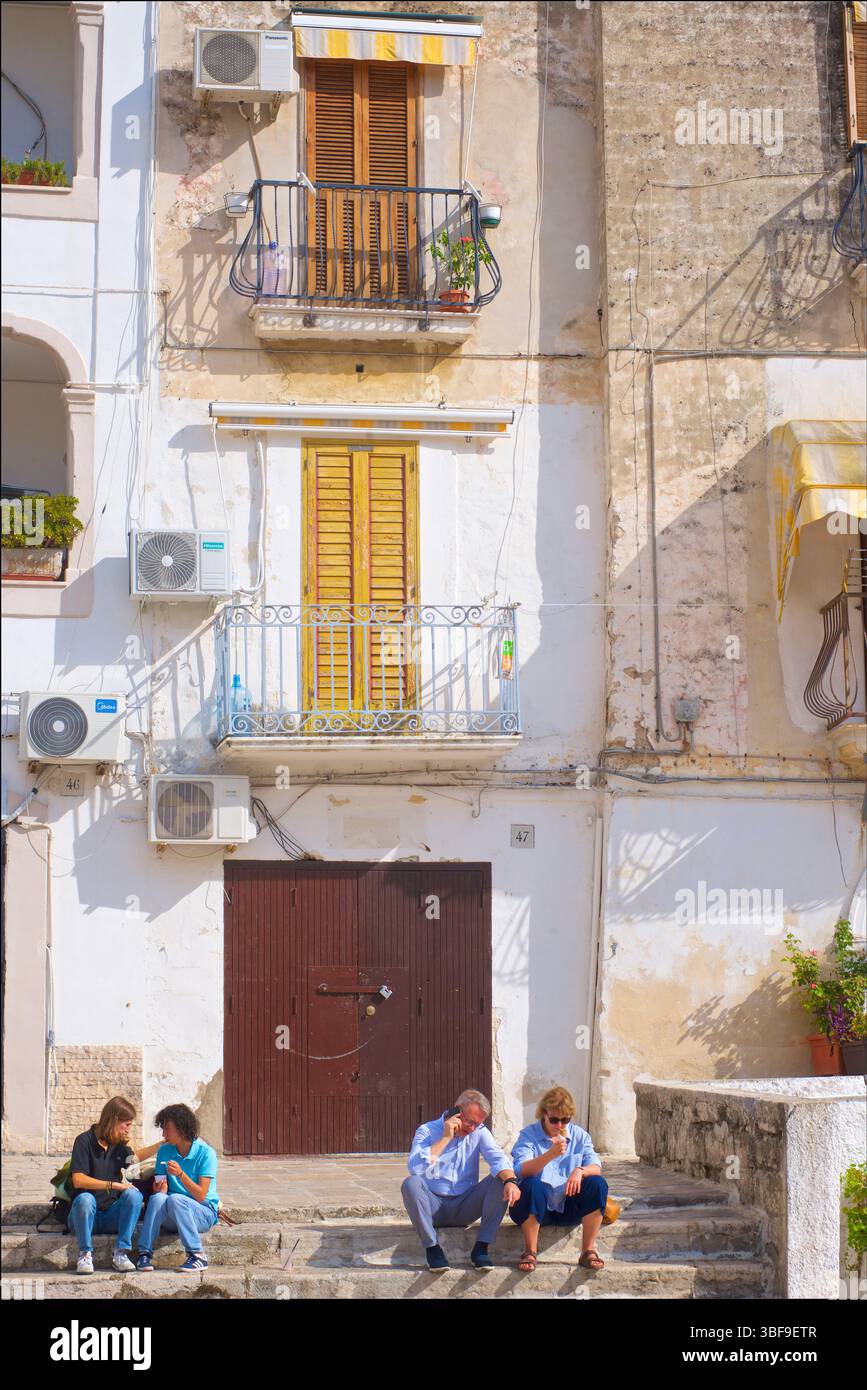 Piazza Federico II di Svevia, Bari, Puglia, Italia. Due coppie sedute sui gradini a mangiare gelato e a parlare al telefono. Foto Stock