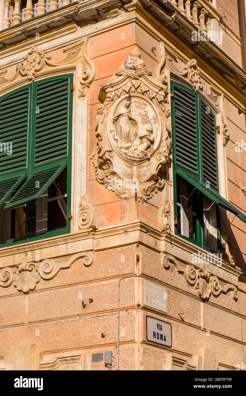 Dettaglio architettonico all'angolo di un edificio in via Roma, oltre alla piazza con la chiesa di San Giovanni Battista, finale Ligure, Italia. Ornamento a bassorilievo con un'iscrizione cristiana in latino: Sint oculi tui aperti super domum hanc traducibile in: Che i vostri occhi siano aperti verso questa casa. Foto Stock
