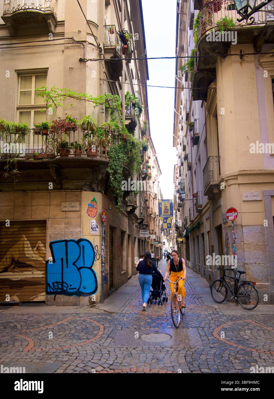 Una scena urbana di strada, nel centro di Torino, in Italia. Ciclista e pedoni in una strada acciottolata. Torino, Italia Foto Stock