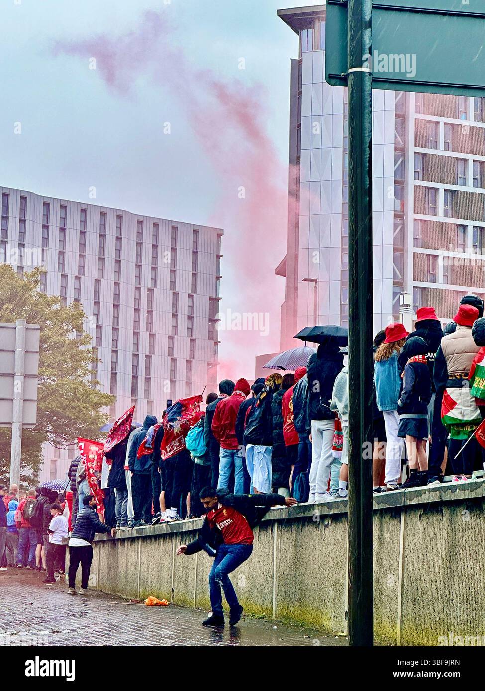I fan si alzano sul muro sotto la pioggia con il fumo rosso che sale mentre aspettano la parata della vittoria di Liverpool su Hunter Street, il 25 maggio 2025 - Immagine stock catturata con smartphone
