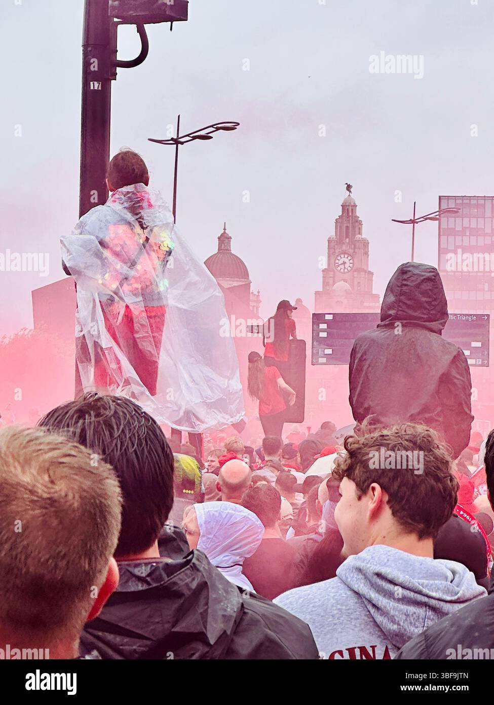 La folla si riunisce sullo Strand durante la parata di Liverpool, ragazze sui lampioni con fumo rosso e Liver Building in background, 25 maggio 2025 - Immagine stock catturata con smartphone