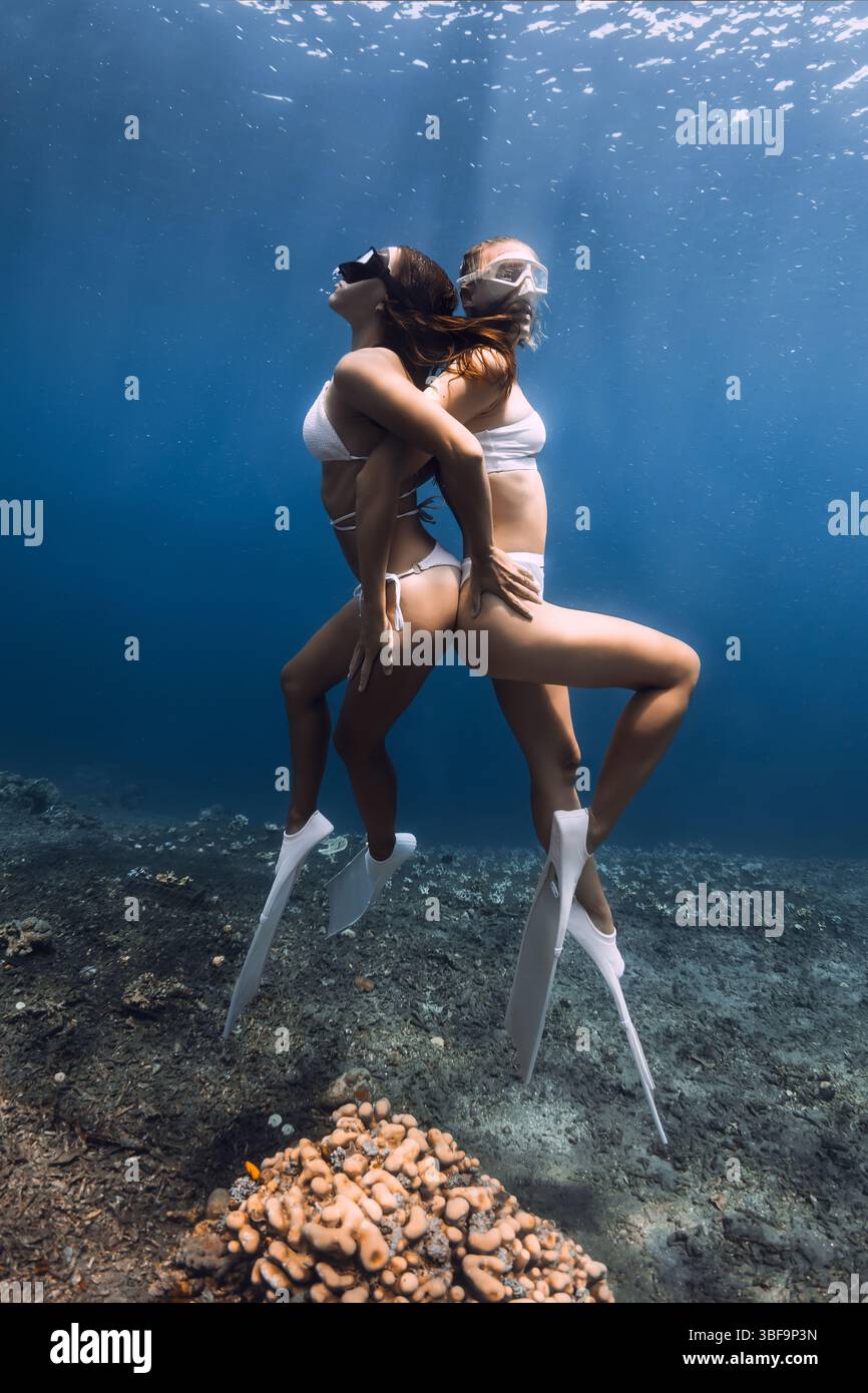Due donne di bellezza in bikini che si tuffano con grazia sott'acqua, nuotano in armonia con le pinne in un oceano limpido. Foto Stock