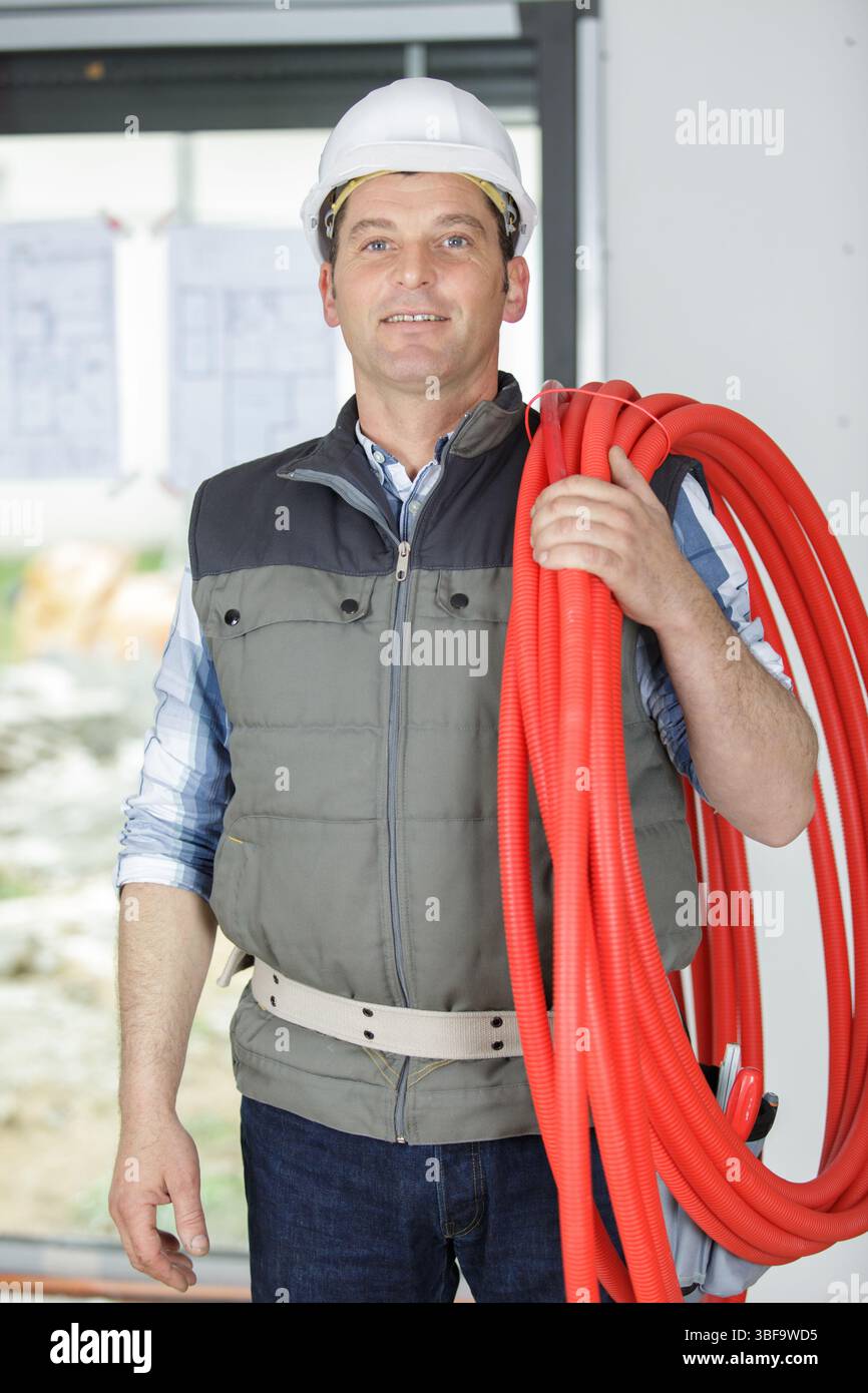 costruttore maturo che regge il tubo flessibile rosso Foto Stock