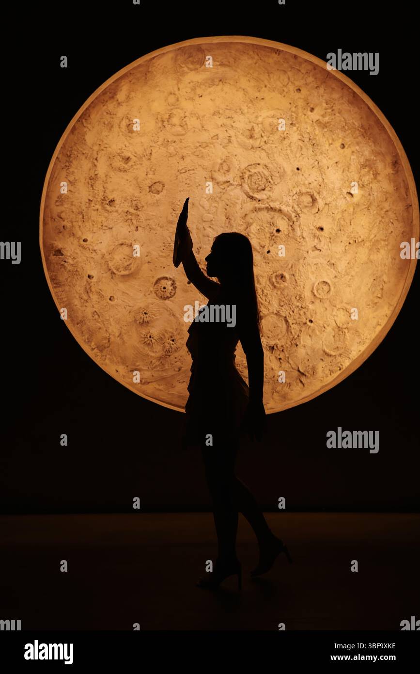 Una graziosa silhouette di ballerini si distingue sullo sfondo mozzafiato di una grande luna Foto Stock