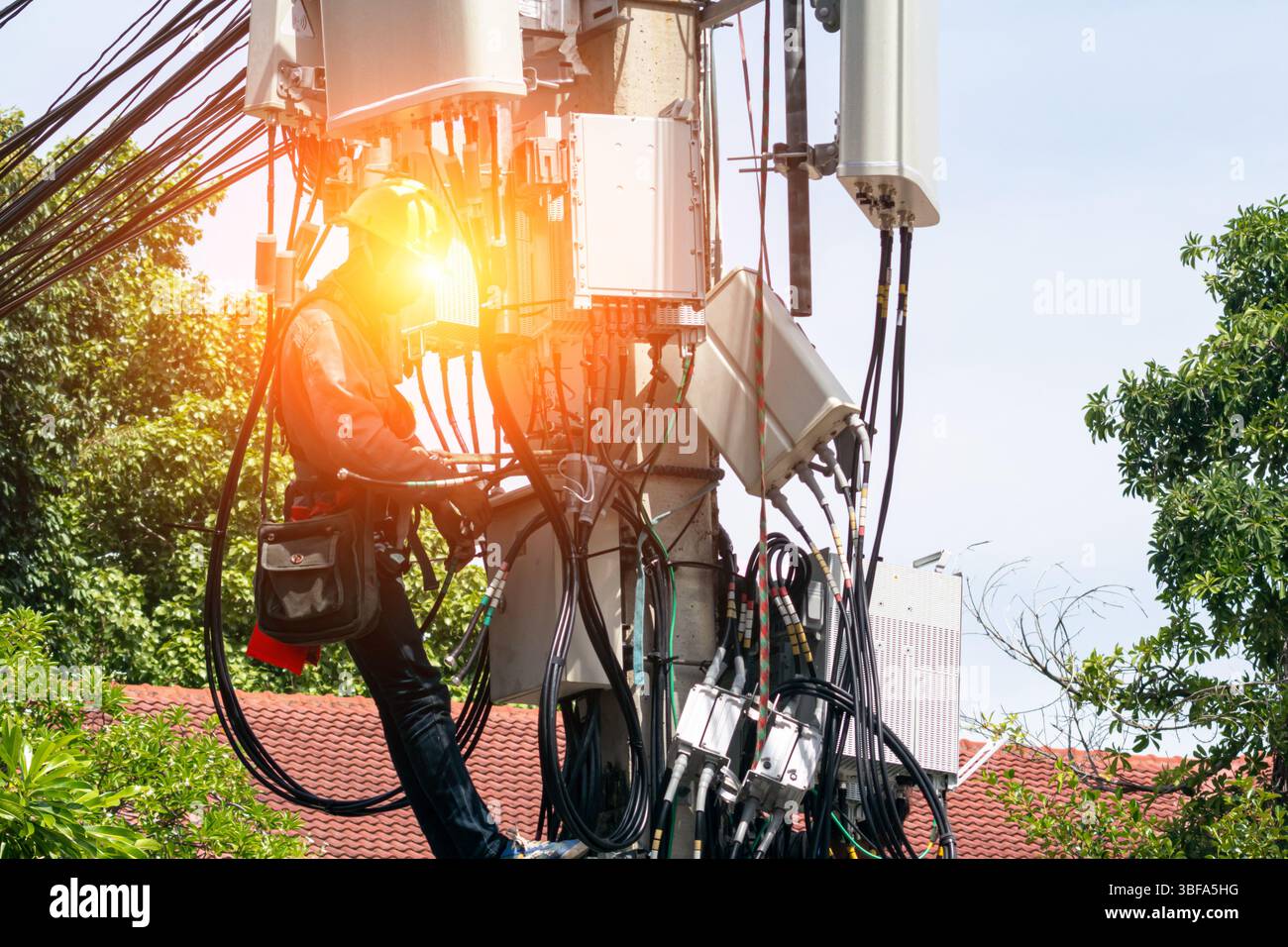 Un tecnico esegue interventi di manutenzione su un'alta torre di comunicazione in mezzo a una città, mostrando manodopera qualificata nelle telecomunicazioni e nelle infrazioni Foto Stock