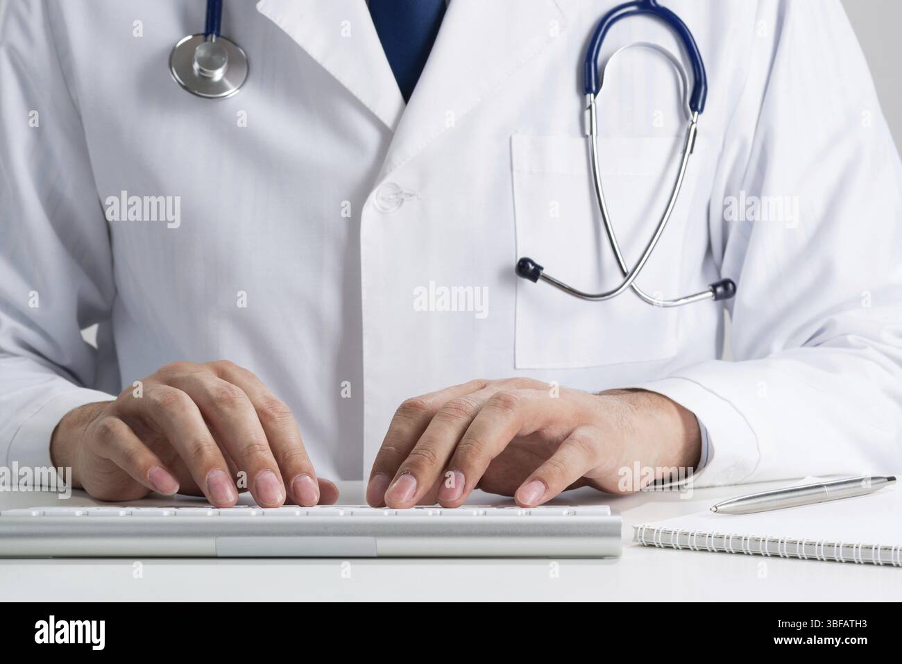 Il terapista maschile sta digitando alla tastiera del computer wireless. Medico in uniforme medica con stetoscopio che lavora con il computer alla scrivania. Tecnologia moderna in Foto Stock