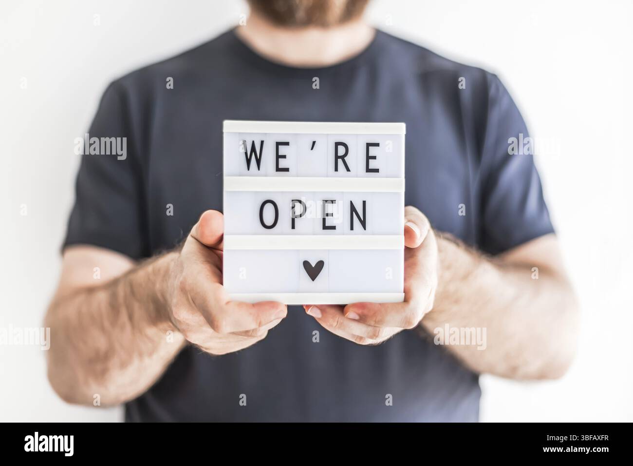 Fine della quarantena. Uomo che tiene la scatola luminosa con messaggio di testo di saluto Siamo aperti nelle sue mani. Hotel, caffetteria, negozio locale, proprietario del servizio che accoglie gli ospiti af Foto Stock
