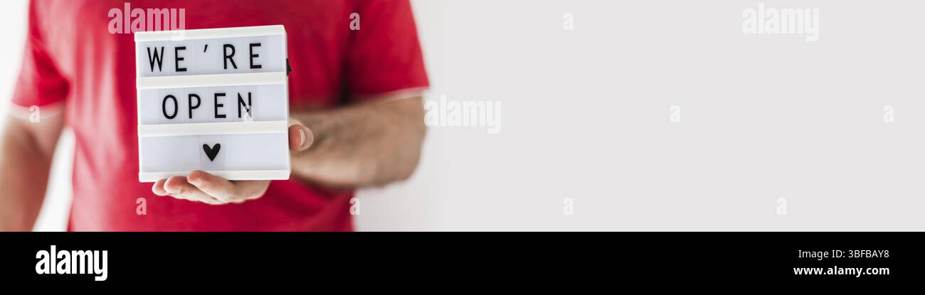 Fine della quarantena. Uomo che tiene la scatola luminosa con messaggio di testo di saluto Siamo aperti nelle sue mani. Hotel, caffetteria, negozio locale, proprietario del servizio che accoglie gli ospiti af Foto Stock