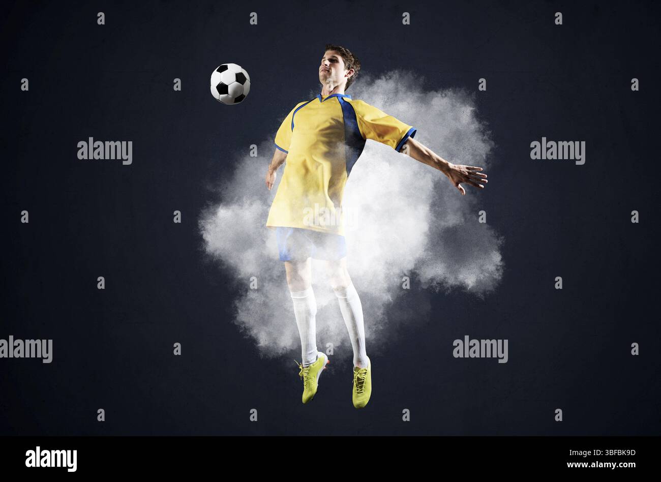 Giocatore di calcio che salta con la palla in fumo. Sportsman in divisa gialla e blu in azione. Concetto di campionato di calcio con spazio copia. Gioco giovane Foto Stock Giocatore di calcio che salta con la palla in fumo. Sportsman in divisa gialla e blu in azione. Concetto di campionato di calcio con spazio copia. Gioco giovane Foto Stock