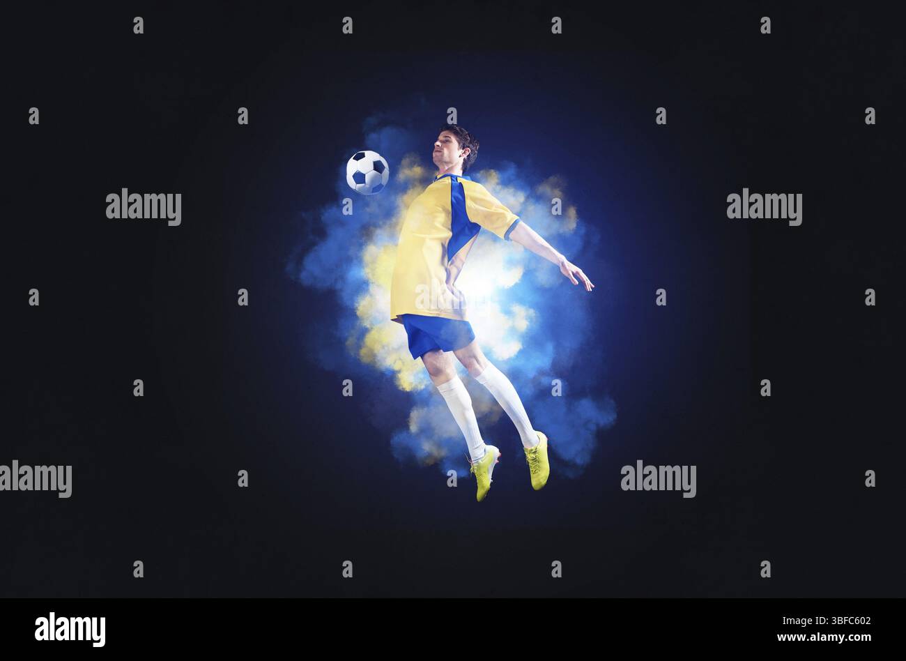 Giocatore di calcio che salta con la palla in fumo. Sportsman in divisa gialla e blu in azione. Concetto di campionato di calcio con spazio copia. Gioco giovane Foto Stock Giocatore di calcio che salta con la palla in fumo. Sportsman in divisa gialla e blu in azione. Concetto di campionato di calcio con spazio copia. Gioco giovane Foto Stock