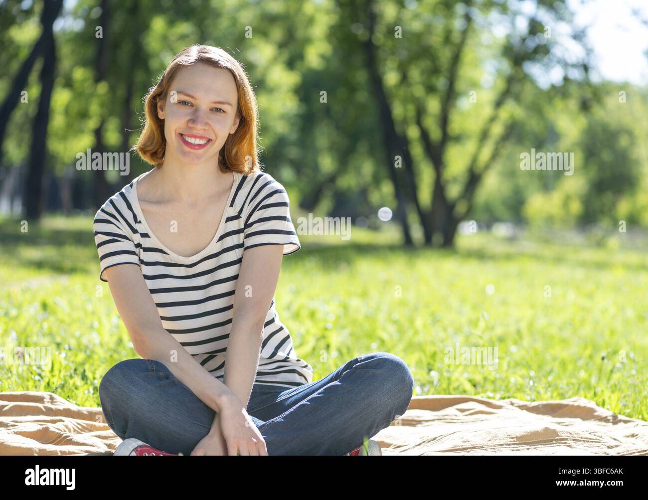 Ritratto di una giovane donna attraente. Seduto a gambe incrociate nel parco Foto Stock