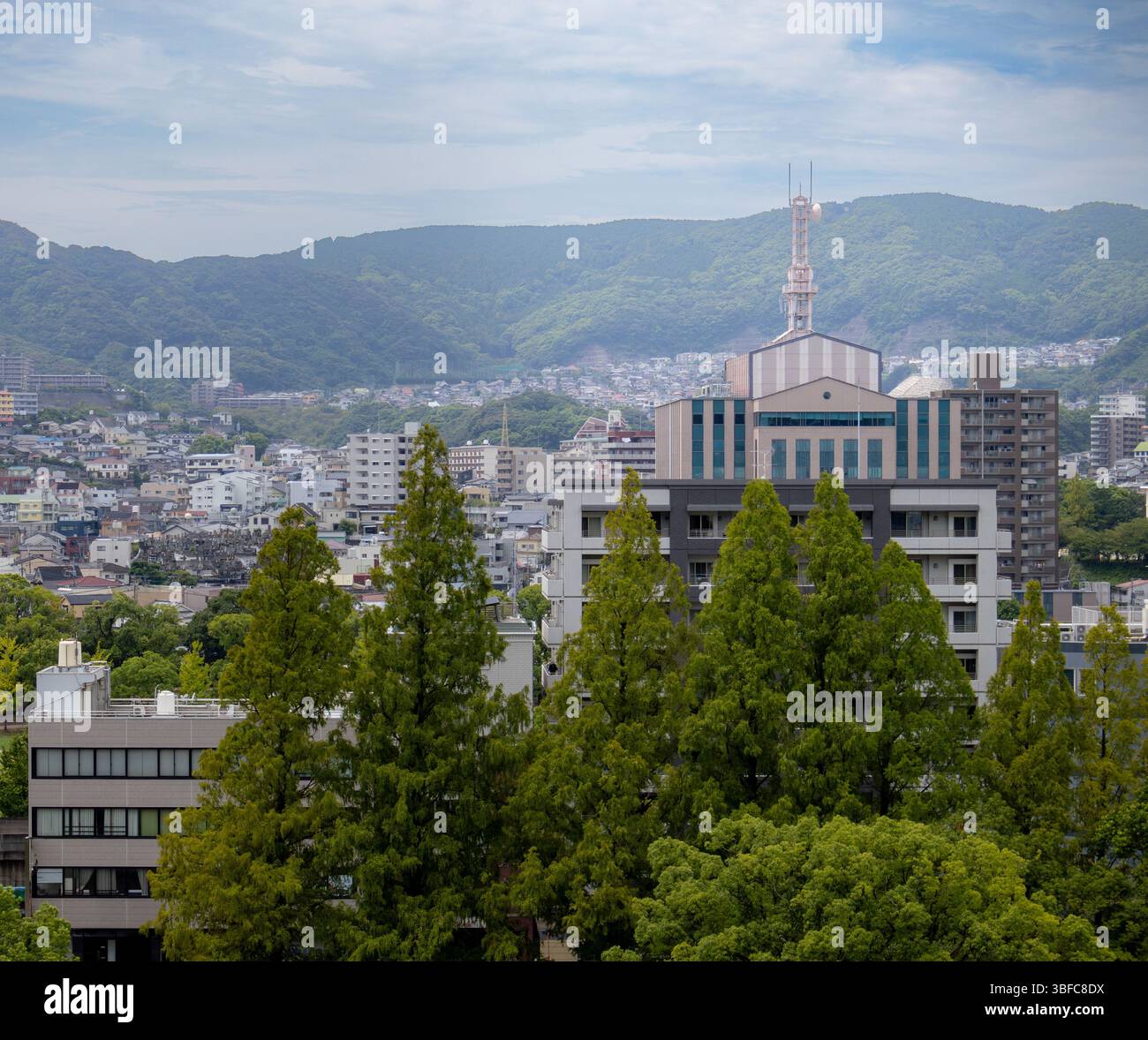 Gli edifici della città giapponese di Nagasaki sono circondati da lussureggianti alberi e montagne. Foto scattata in una giornata nuvolosa Foto Stock