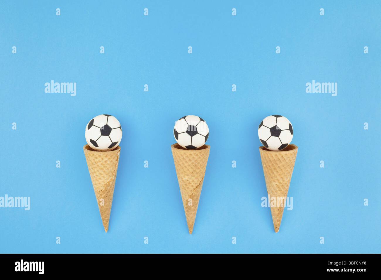 Creative laici piatta vista dall'alto di gelati i coni di cialda con palloni da calcio macarons in bright bold sfondo blu con copia spazio in stile minimal, conce Foto Stock