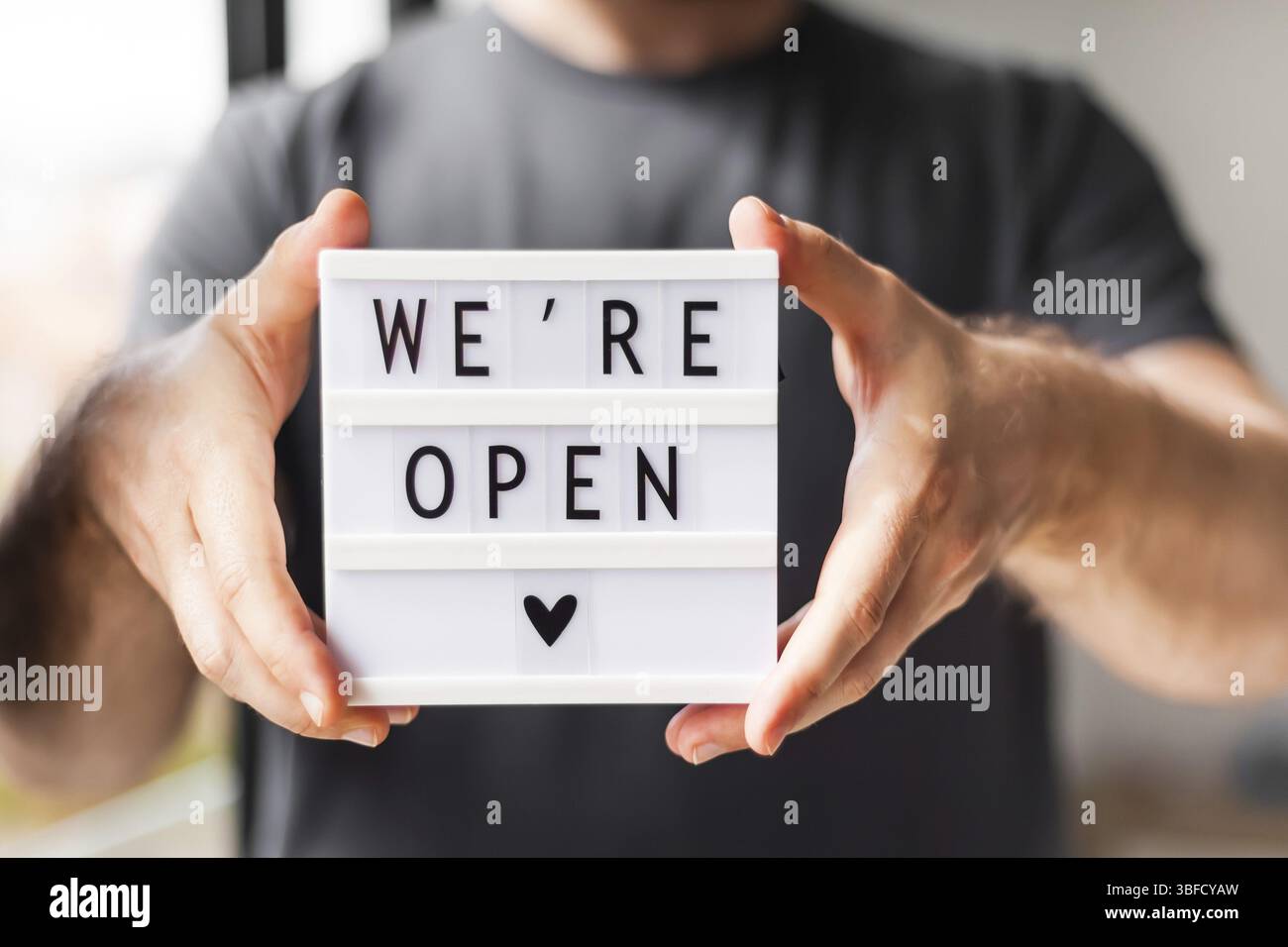 Fine della quarantena. Uomo che tiene la scatola luminosa con messaggio di testo di saluto Siamo aperti nelle sue mani. Hotel, caffetteria, negozio locale, proprietario del servizio che accoglie gli ospiti af Foto Stock