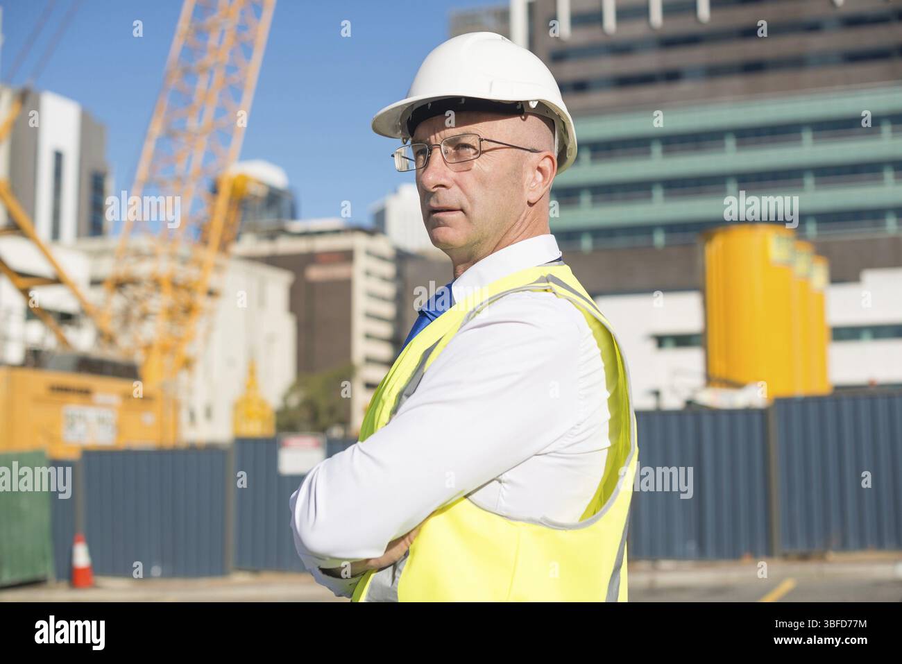 Fiducioso tecnico delle costruzioni in hardhat con le braccia incrociate sul petto Foto Stock